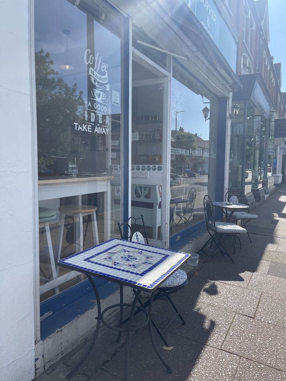 The KOZY shopfront window seen from the pavement, with a tiled bistro table and chairs outside in the sun